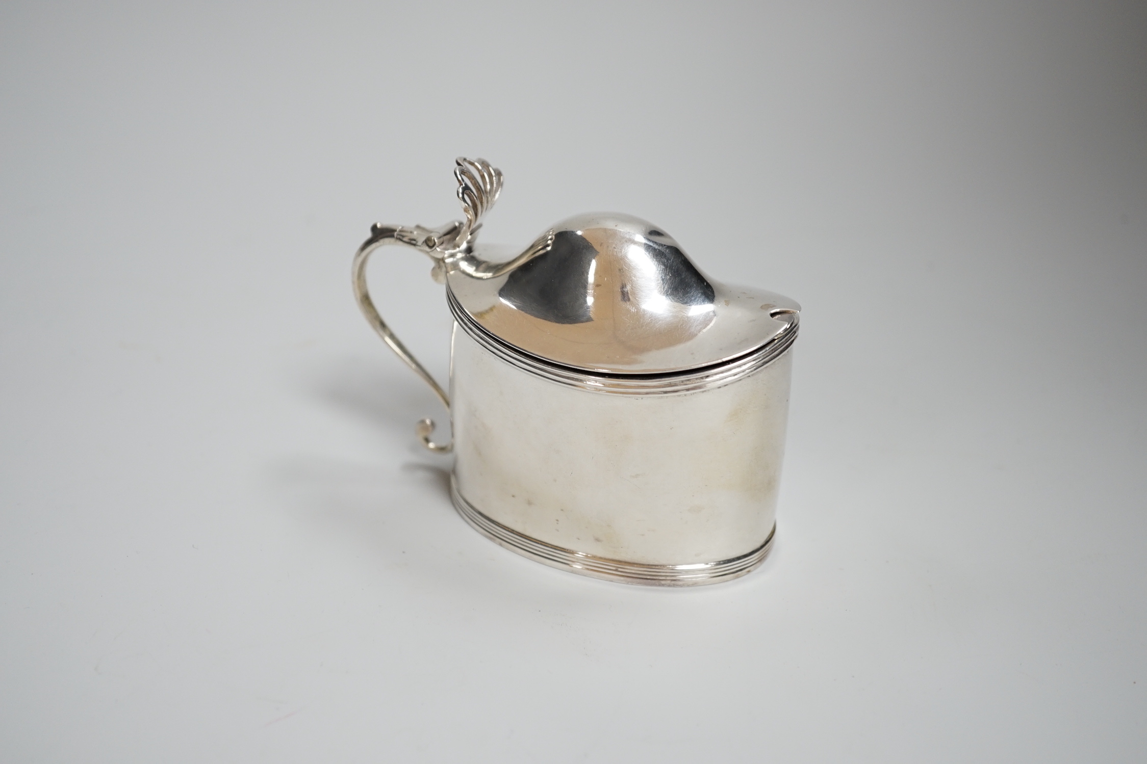 A George III oval silver drum mustard, with domed cover, glass liner and plated spoon, makers Peter, Anne and William Bateman, London 1800, 121 grams